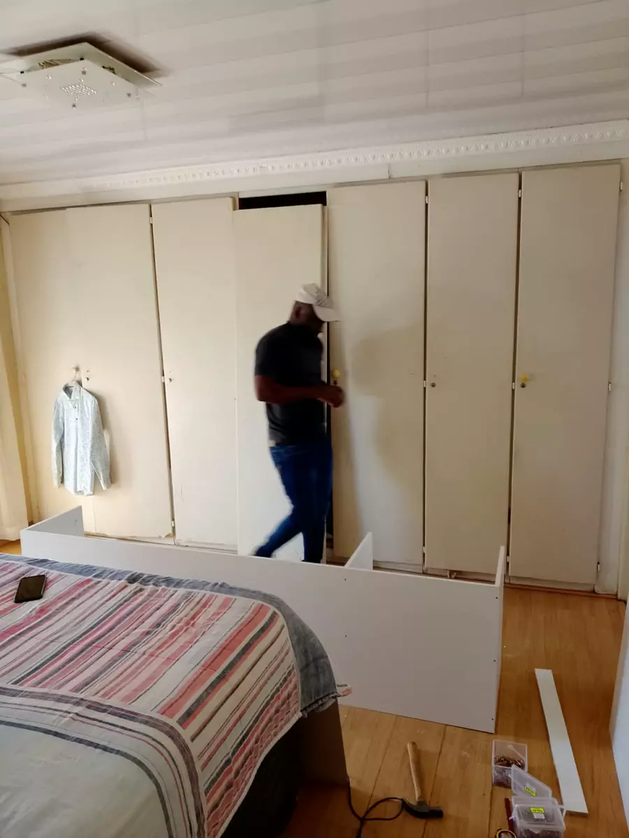 Man assembling furniture in a bedroom with built-in wardrobes