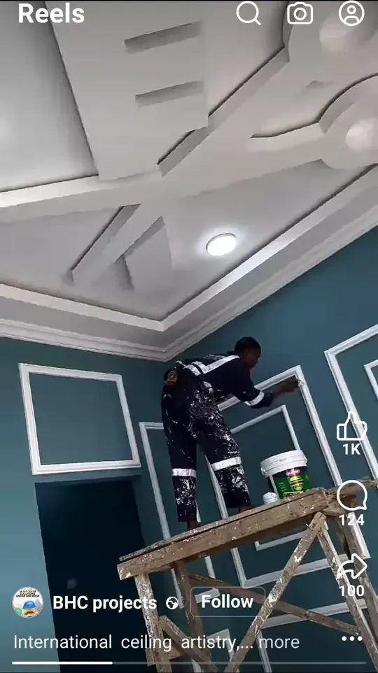 Low-angle shot of a worker on scaffolding painting wall moldings