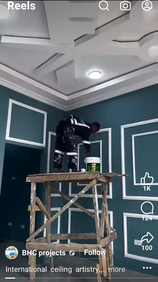 Worker standing on wooden scaffold in a teal room with white ceiling design